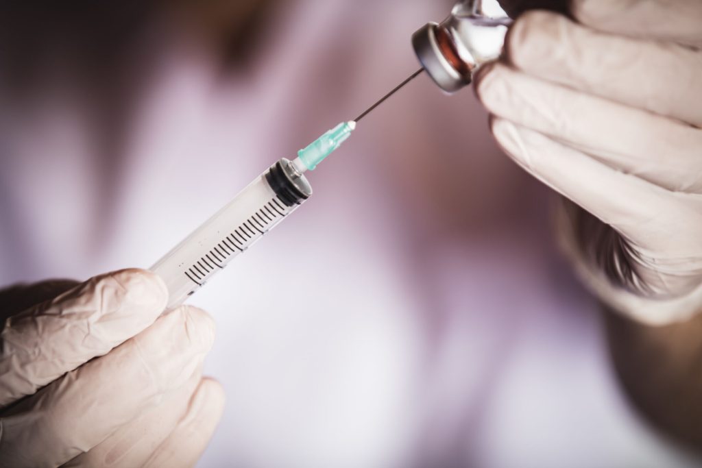 Health worker drawing vaccine in vial into syringe for COVID-19, measles, flu shots